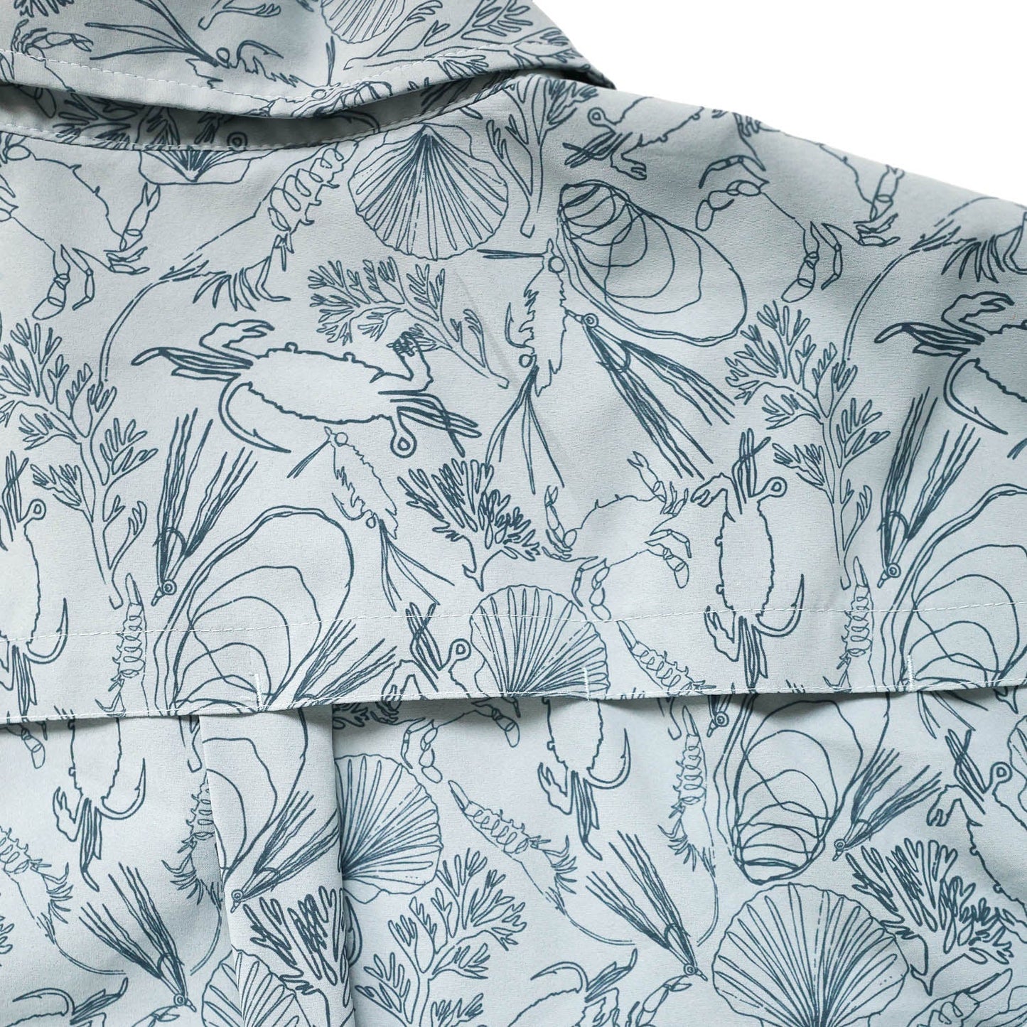 Close-up of light blue fabric with marine life pattern featuring crabs, shells, and seaweed and fishing flies showing the ventilated back of the shirt .