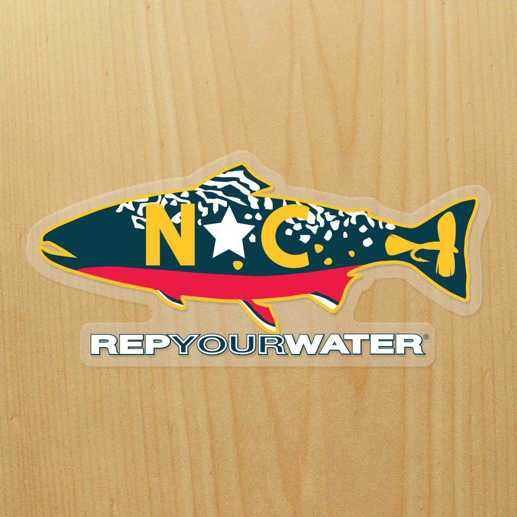 A wood background has a sticker on it that is a brook trout with NC in the middle of it and a fly in the tail. It reads RepYourWater underneath the trout