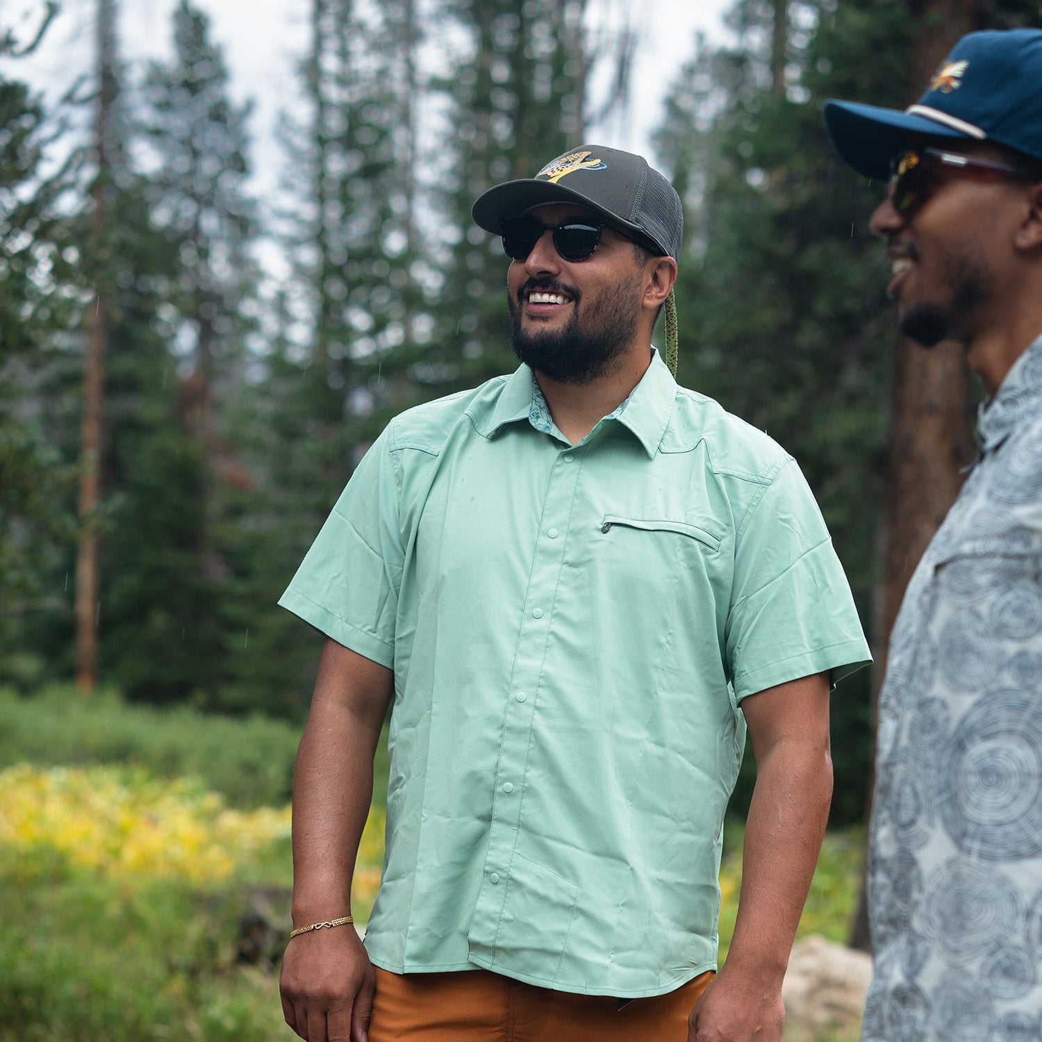 Two men standing outdoors with a forest background
