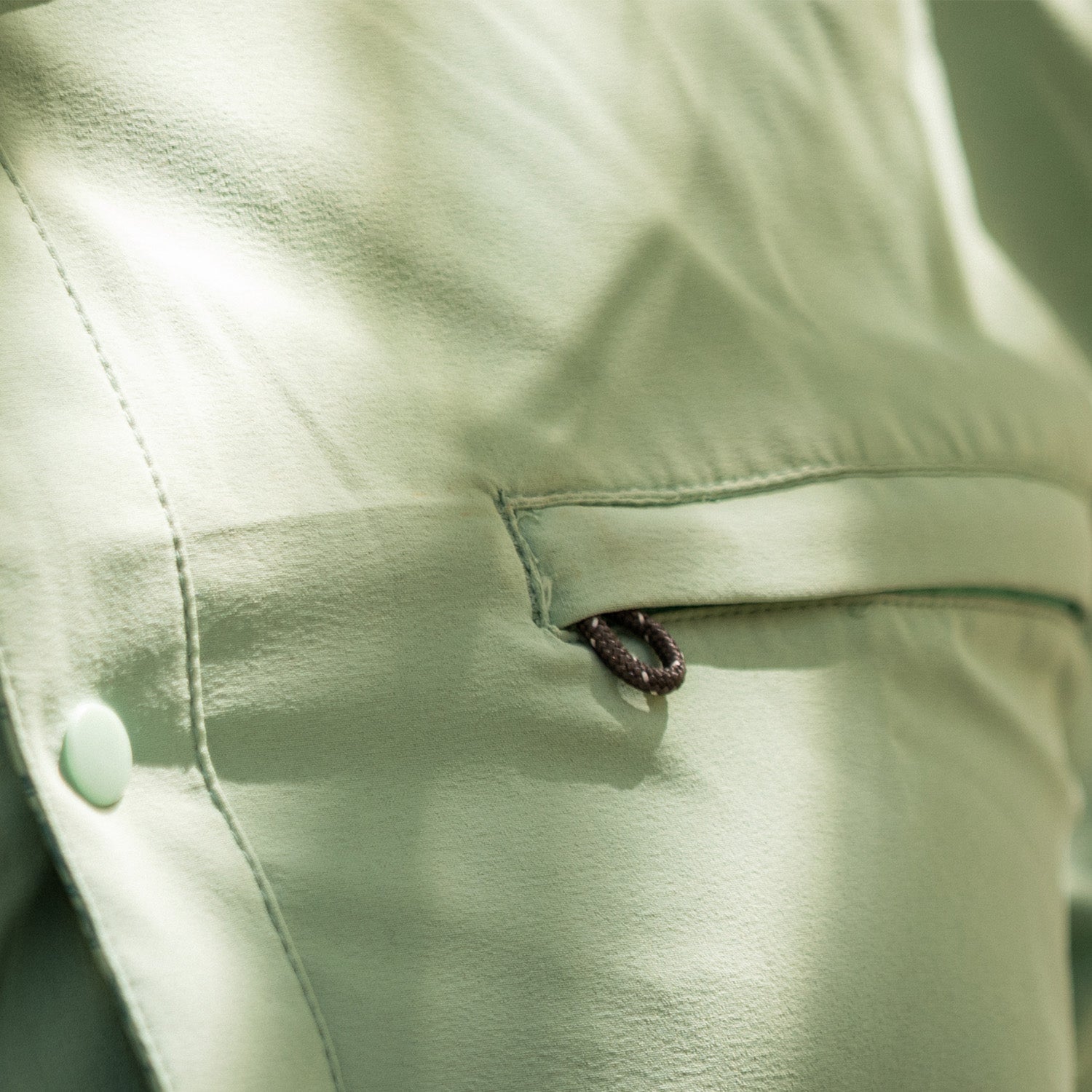 Close-up of a light green shirt with a button and zipper detail.