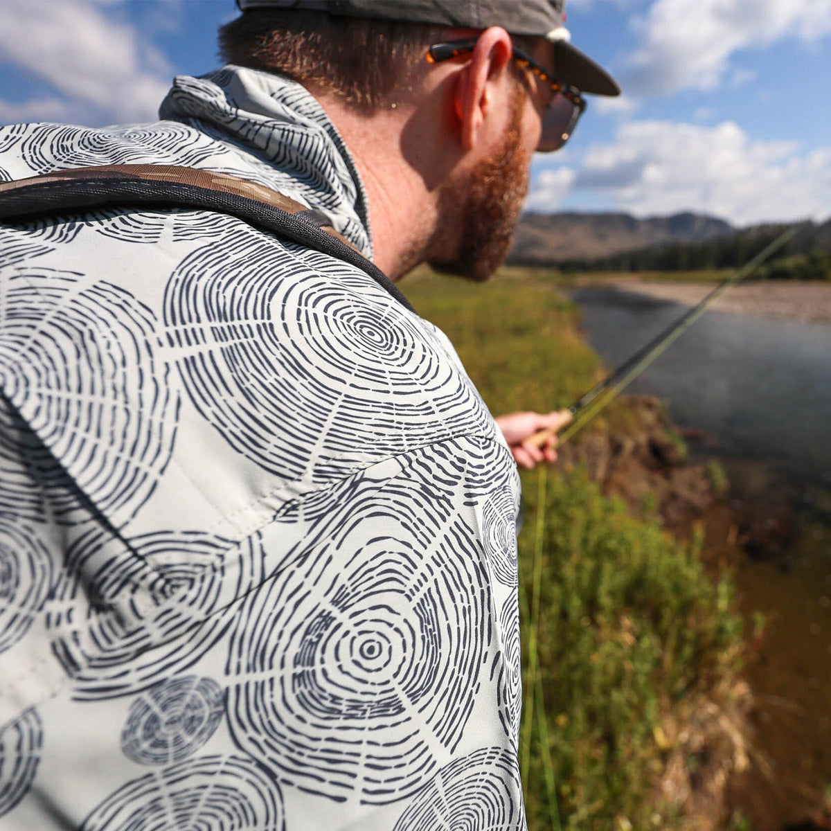 man fishing on a river wearing a tree ring pattern deschutes button down shirt 
