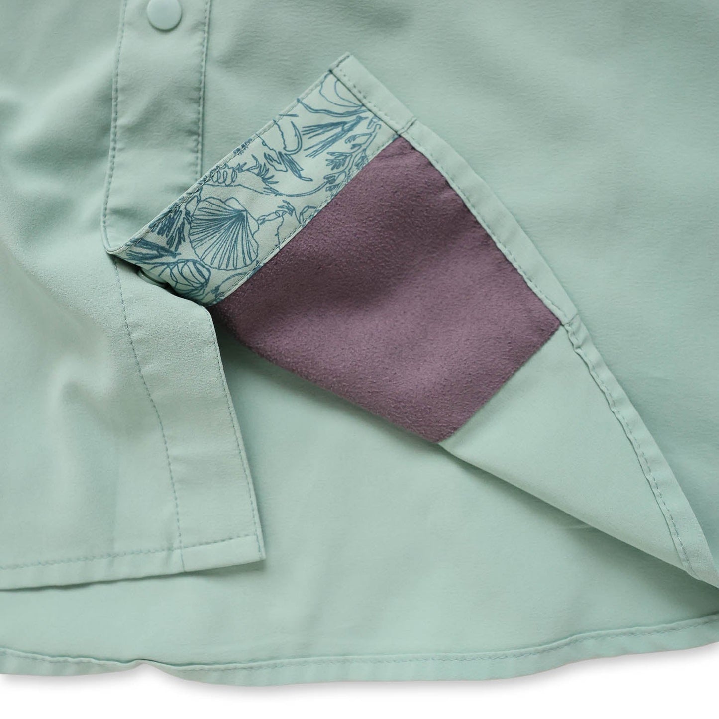 Close-up of a light green/cenote  button down shirt with a sea floor doodle lining and sunglass wipe on a white background