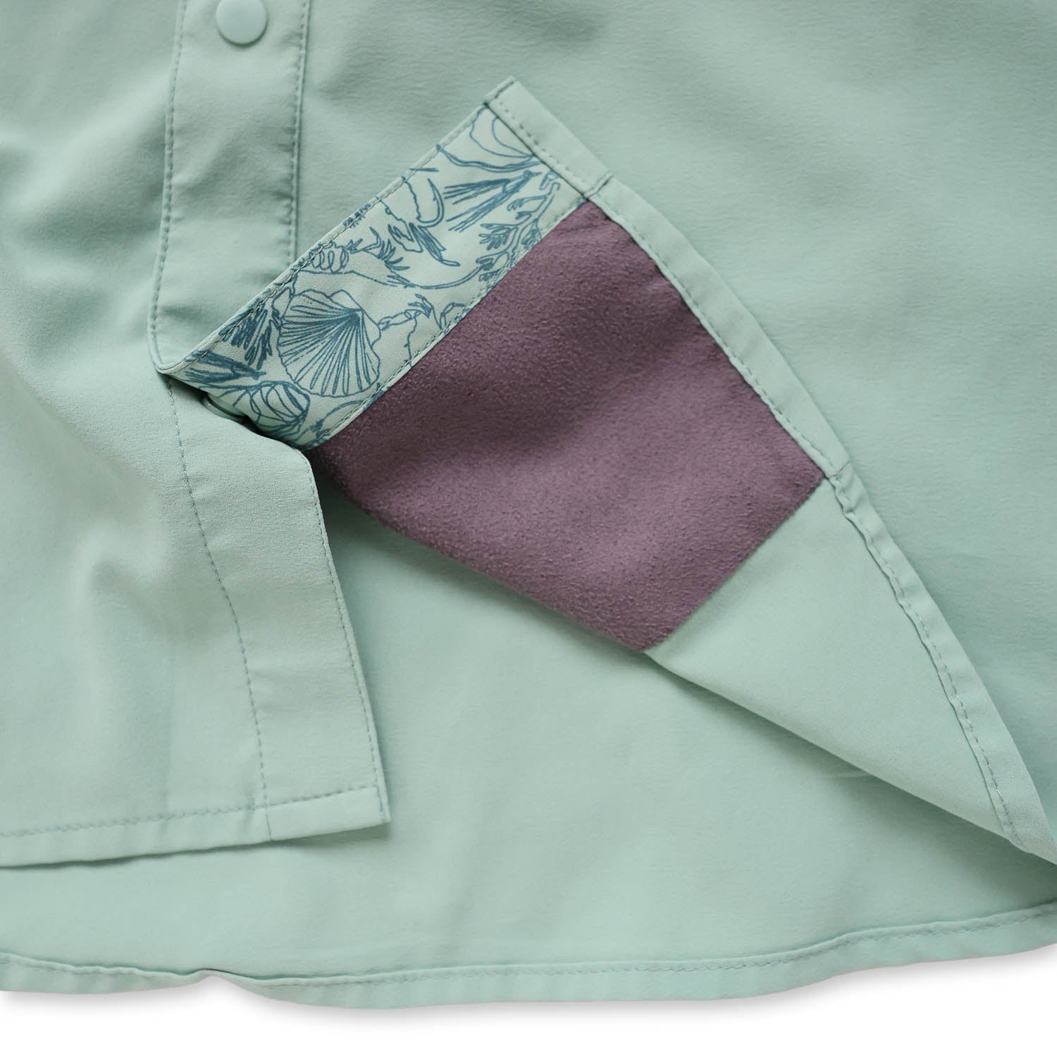 Close-up of a light green/cenote  button down shirt with a sea floor doodle lining and sunglass wipe on a white background
