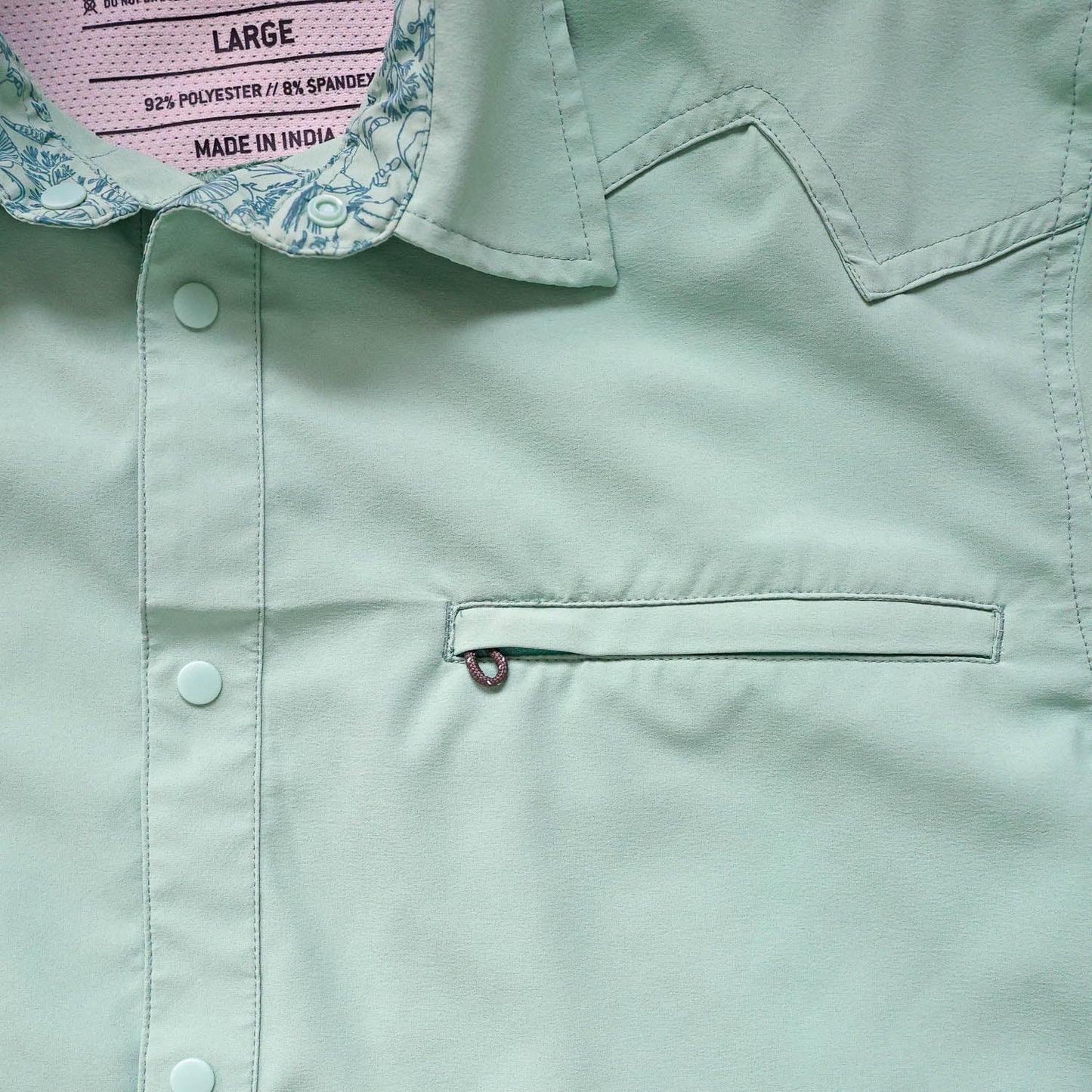 Close-up of a light green/cenote  button down shirt with a sea floor doodle lining collar and chest pocket 