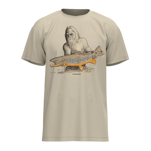 Tan tee shirt with a drawing of sasquatch holding a brown trout on the front