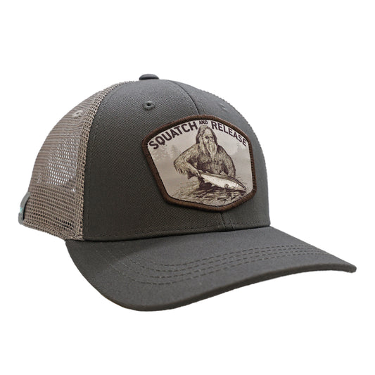 A hat with gray mesh back and gray front. The front features a design with sasquatch releasing a fish with mountains that says squatch and release.