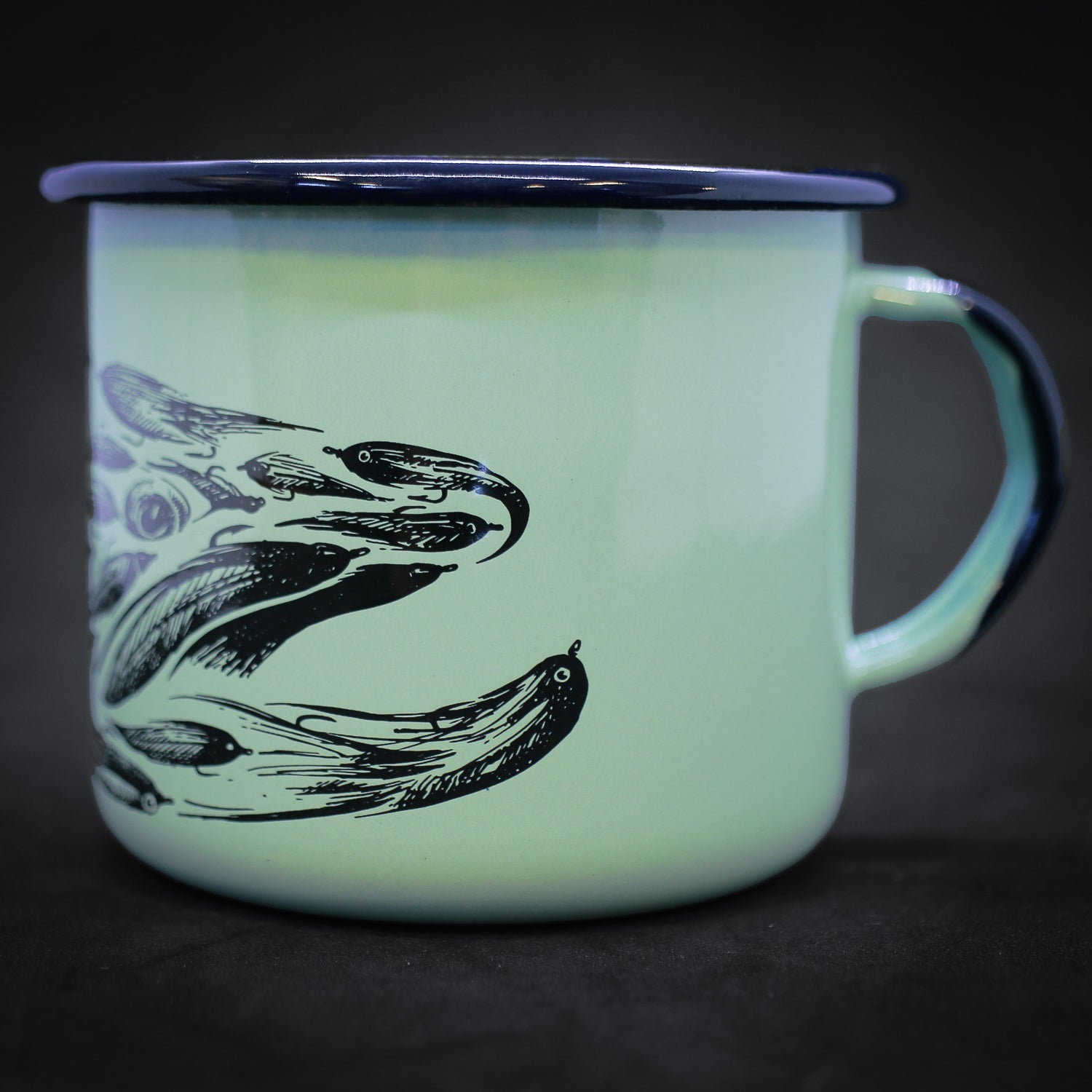 Photo of a teal ceramic mug with hints of royal blue with a pen and ink drawing of a trout head made up of fishing flies