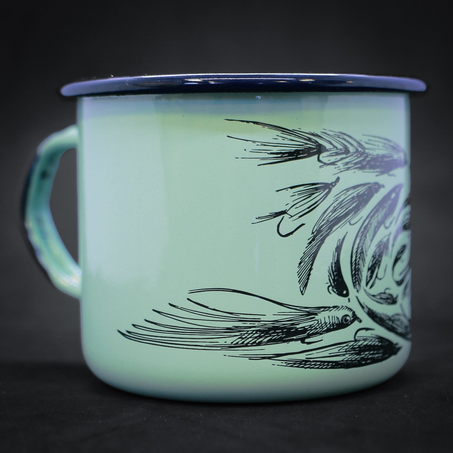 Photo of a teal ceramic mug with hints of royal blue with a pen and ink drawing of a trout head made up of fishing flies